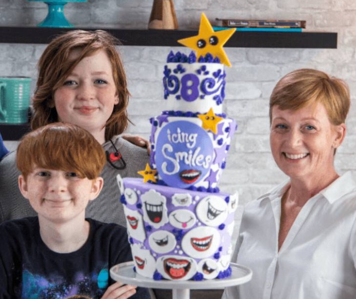 a boy and two women posing around a cake