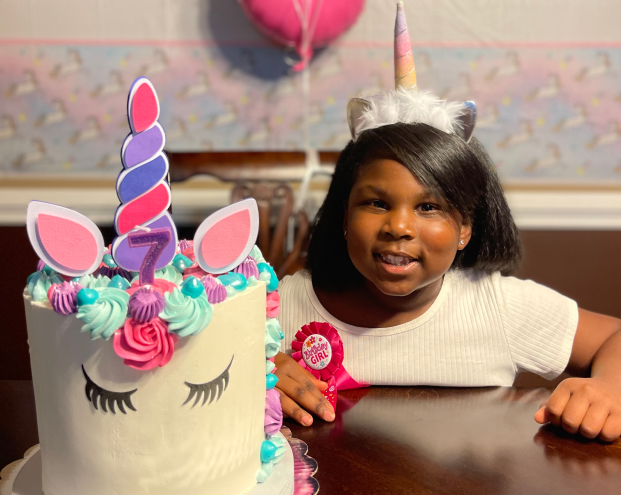 girl in unicorn hat smiling with a unicorn cake