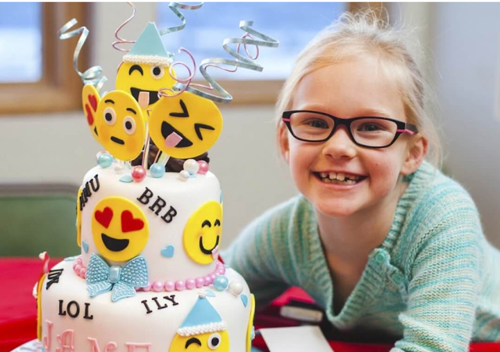 girl smiling with an emoji cake