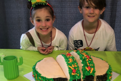 two kids next to a taco cake